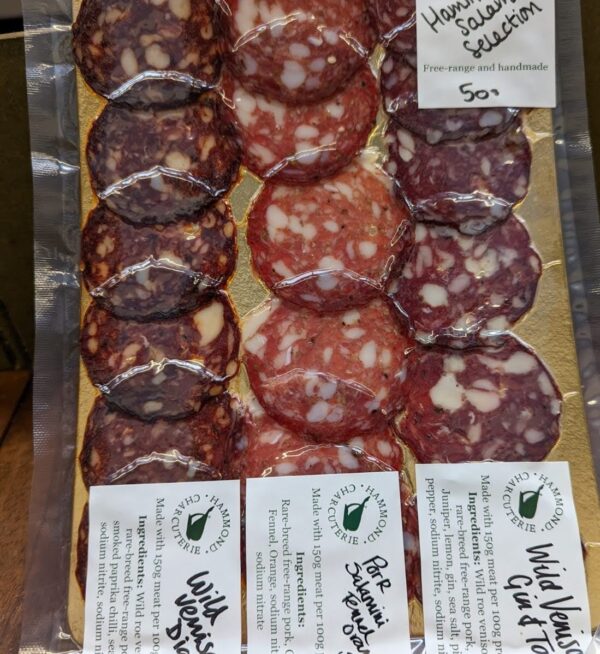 A vac pack of sliced salami filling a gold board, three colours of salami and labels showing each variety
