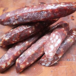 pheasant salami with a little pork fat on a handsome wooden chopping board. The salami is a rich colour